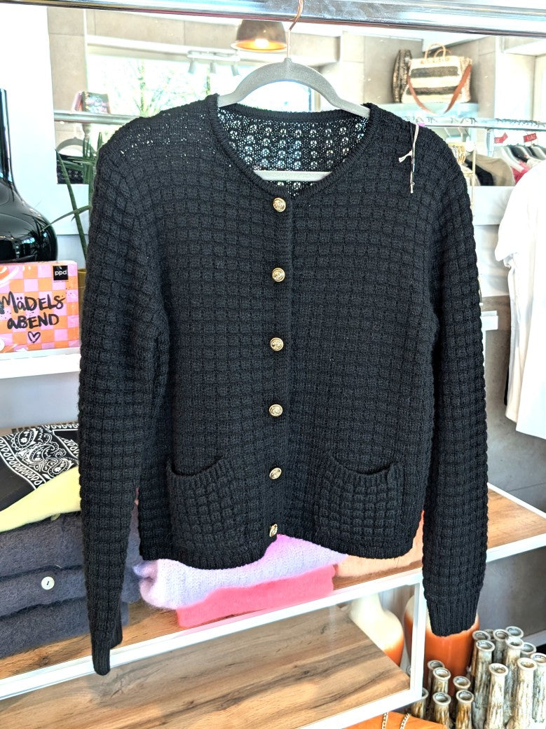 Die schwarze Cardigan-Strickjacke im Chanel-Stil mit ihren markanten Quadrate und edlen Goldknöpfen vereint zeitlose Eleganz mit modernem Komfort!