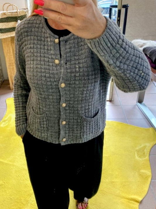 Die graue Cardigan-Strickjacke im Chanel-Stil mit ihren markanten Quadrate und edlen Goldknöpfen vereint zeitlose Eleganz mit modernem Komfort!