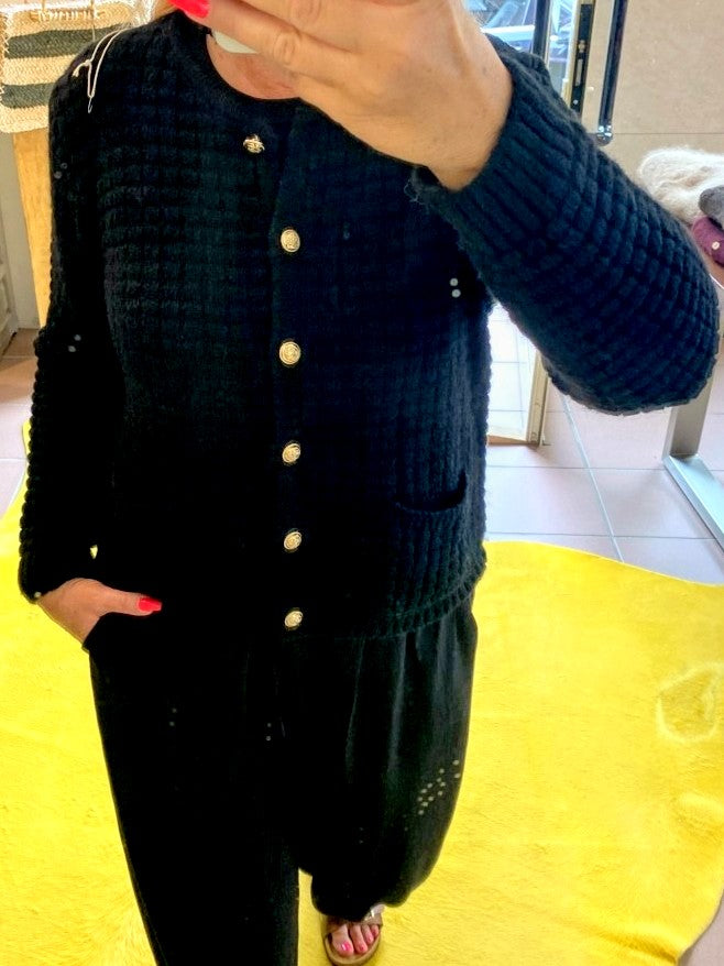 Die schwarze Cardigan-Strickjacke im Chanel-Stil mit ihren markanten Quadrate und edlen Goldknöpfen vereint zeitlose Eleganz mit modernem Komfort!