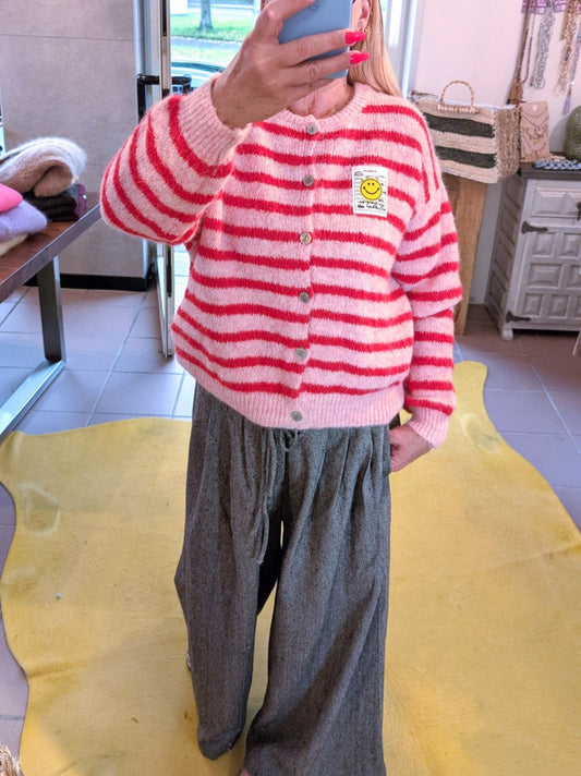 Die gestreifte Cardigan-Strickjacke in fröhlichen Rosa- und Rot-Tönen bringt mit ihrem gelben Smiley-Aufnäher und  Perlmuttknöpfen gute Laune in jeden Look!