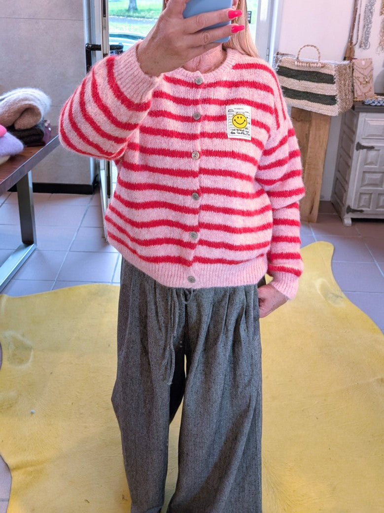 Die gestreifte Cardigan-Strickjacke in fröhlichen Rosa- und Rot-Tönen bringt mit ihrem gelben Smiley-Aufnäher und  Perlmuttknöpfen gute Laune in jeden Look!