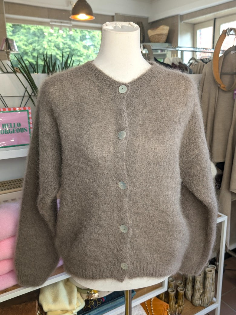 Fühle dich behaglich und stilvoll mit unserer Cardigan Strickjacke aus 80% Soft Kid Mohair Taupe mit hellen Perlmuttknöpfen. Perfekt für alle Gelegenheiten