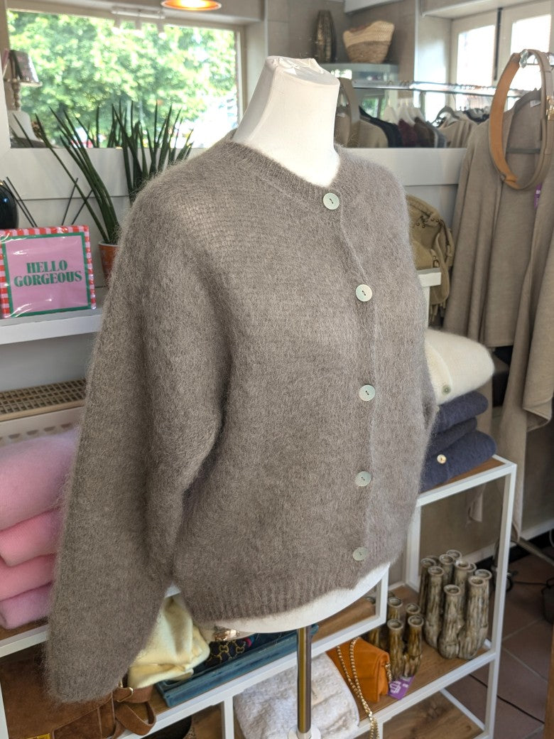 Fühle dich behaglich und stilvoll mit unserer Cardigan Strickjacke aus 80% Soft Kid Mohair Taupe mit hellen Perlmuttknöpfen. Perfekt für alle Gelegenheiten