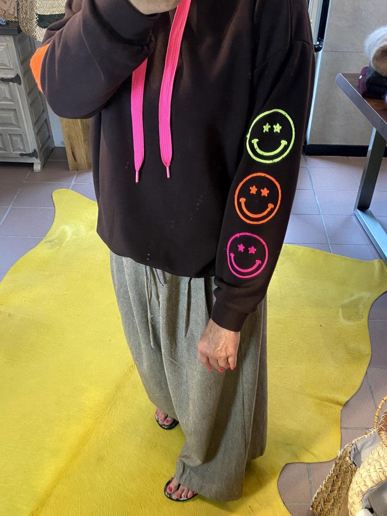 Der Hoodie von AZARA vereint warmes Coffee Braun mit Smileys und Blitzelementen in lebendigem Neon Pink, Orange und Grün in einem einzigartigen Design!