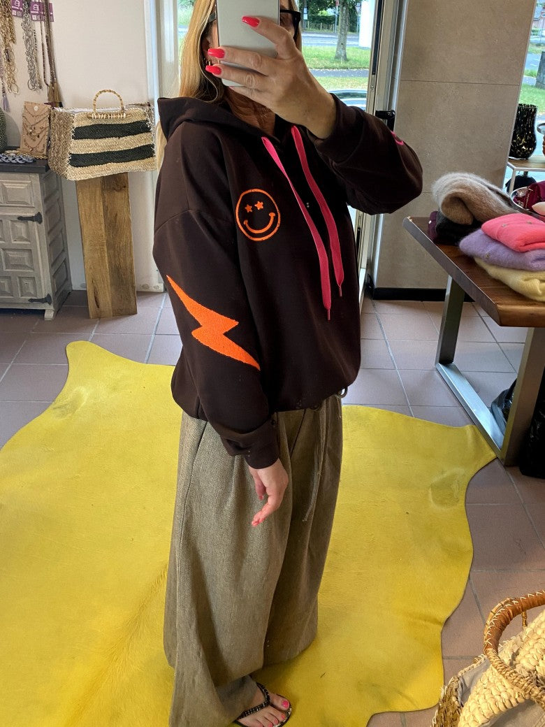 Der Hoodie von AZARA vereint warmes Coffee Braun mit Smileys und Blitzelementen in lebendigem Neon Pink, Orange und Grün in einem einzigartigen Design!