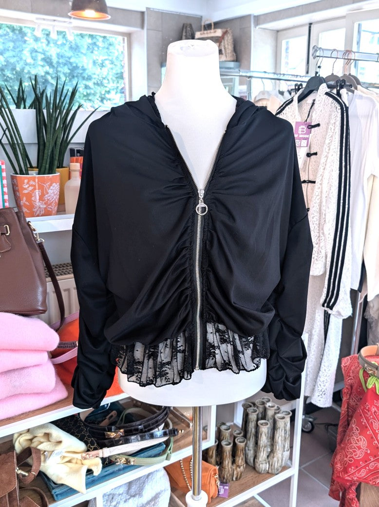 Elegante Jacke aus fließender Viskose in Schwarz mit zartem Spitzensaum, romantischen Rüschenärmeln und praktischer Kapuze - vielseitige Styling-Möglichkeiten.