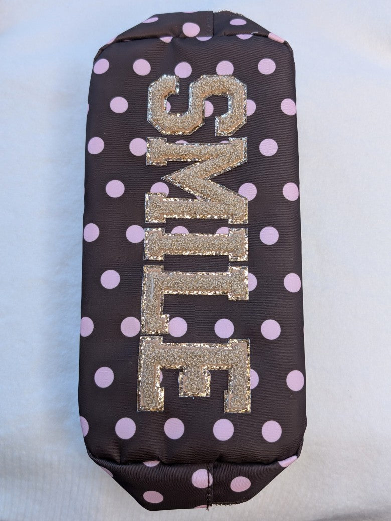 Die Make-Up- und Kosmetiktasche/ Kulturtasche vereint praktische Funktionalität mit trendigem Design in Coffee Braun mit rosa Punkten und "Smile" in Gold!