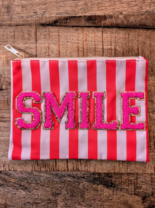 Die Make-Up- und Kosmetiktasche vereint praktische Funktionalität mit fröhlichem Design in gestreiftem Muster Orange Rosa mit "SMILE" in Pink und Gold!