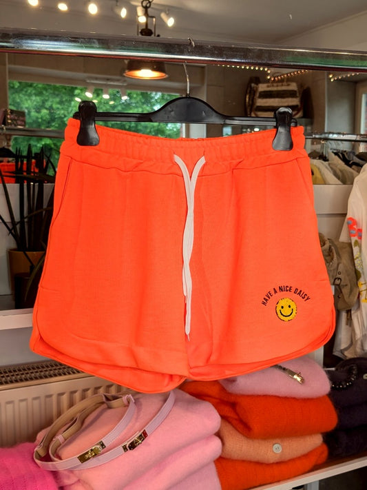 Entdecke den perfekten Sommerlook mit unser "Have A Nice Day" Smiley Shorts in Neon Orange aus bequemem Sweatshirtstoff. Ideal und auffallend für heiße Tage!