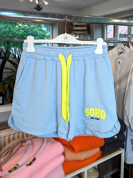 Erwecke den Sommer mit dieser stylischen SOHO Shorts aus Sweatshirtstoff in Hellblau mit Schriftzug in Neon Gelb aus Baumwolle. Perfekt für jeden Anlass!