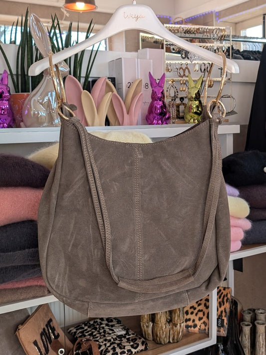 Die elegante Hobo Bag aus hochwertigem Wildleder in Schlamm Dark Taupe mit herausnehmbarer Innentasche besticht durch goldenen Ösen und italienisches Handwerk.