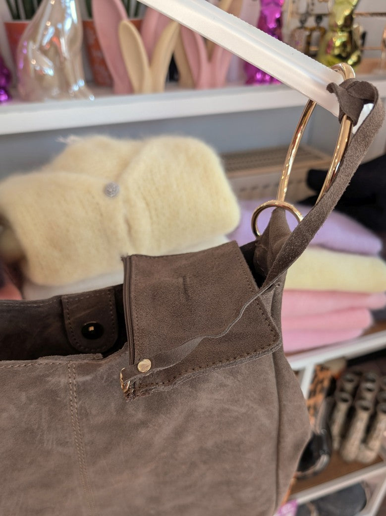 Die elegante Hobo Bag aus hochwertigem Wildleder in Schlamm Dark Taupe mit herausnehmbarer Innentasche besticht durch goldenen Ösen und italienisches Handwerk.